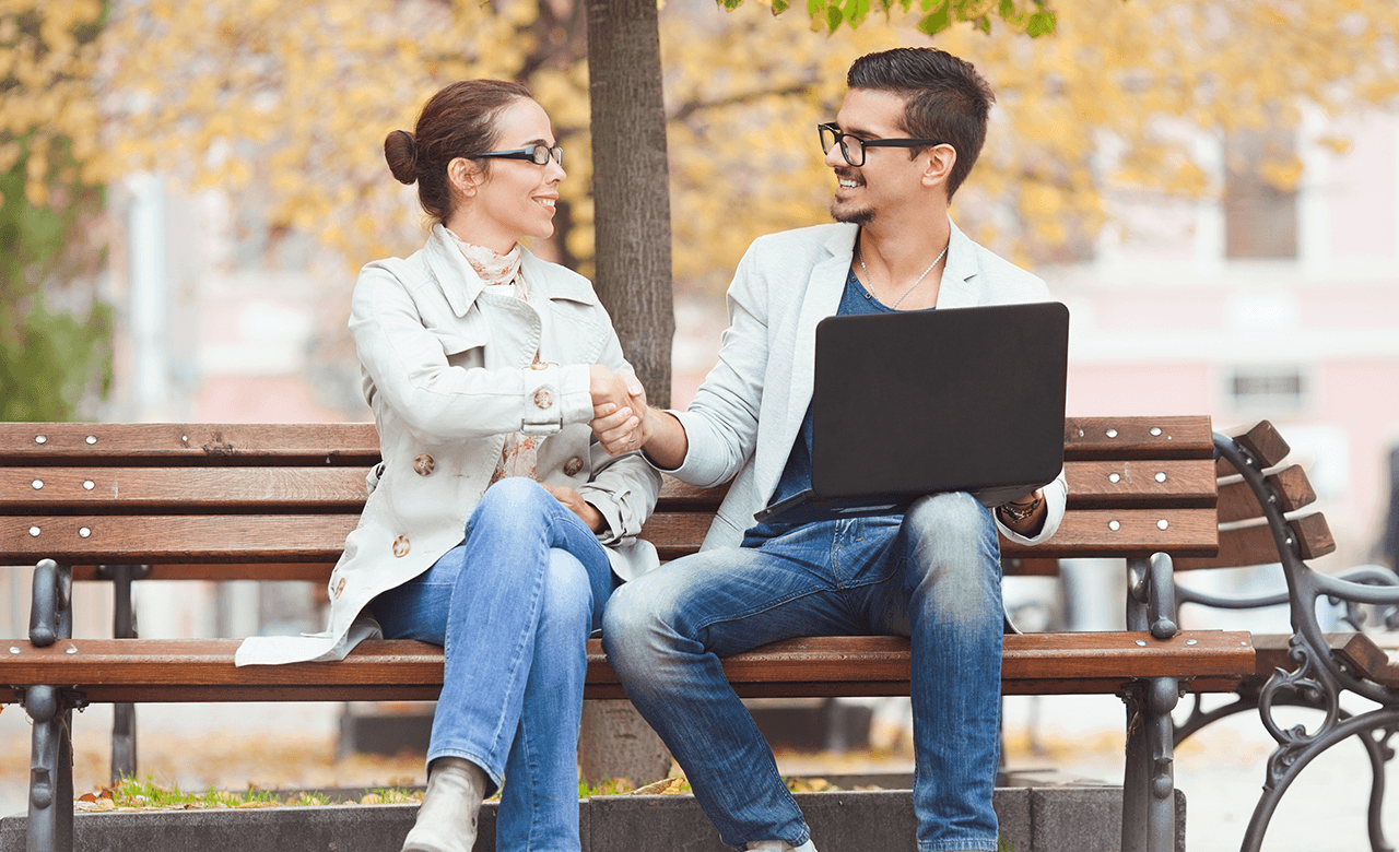 Woman and man with laptop on park bench shaking hands