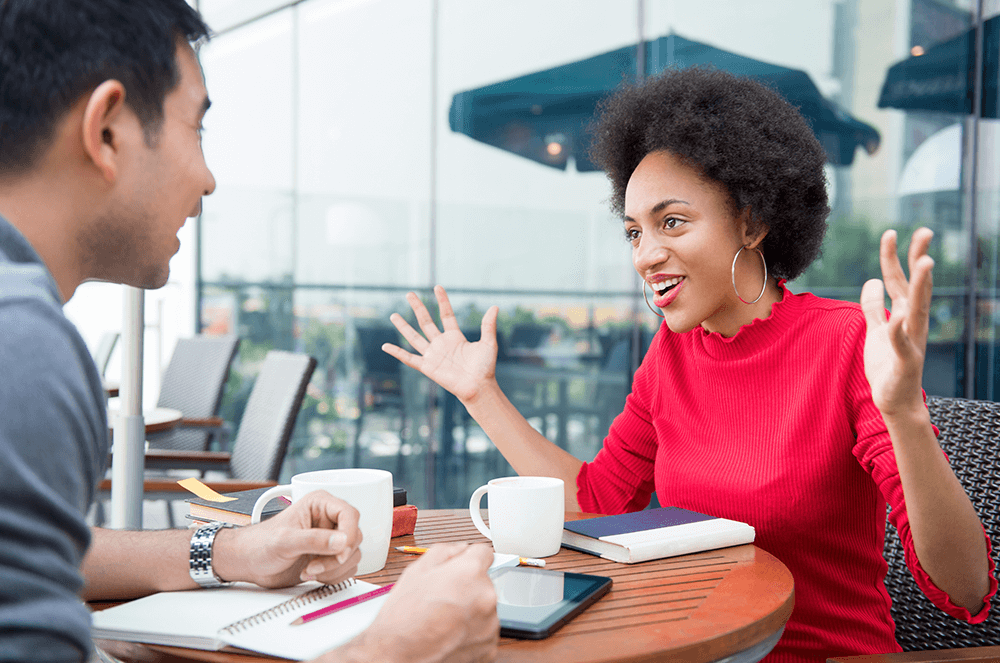 Woman in red shirt speaking to man over coffee