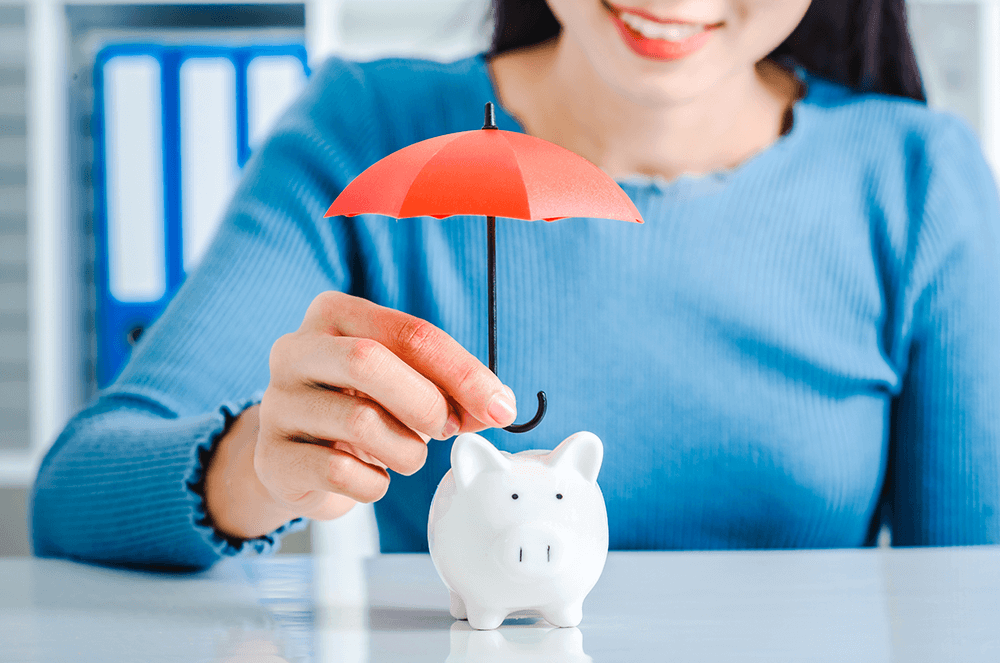 Woman in blue shirt holding small umbrella over piggy bank