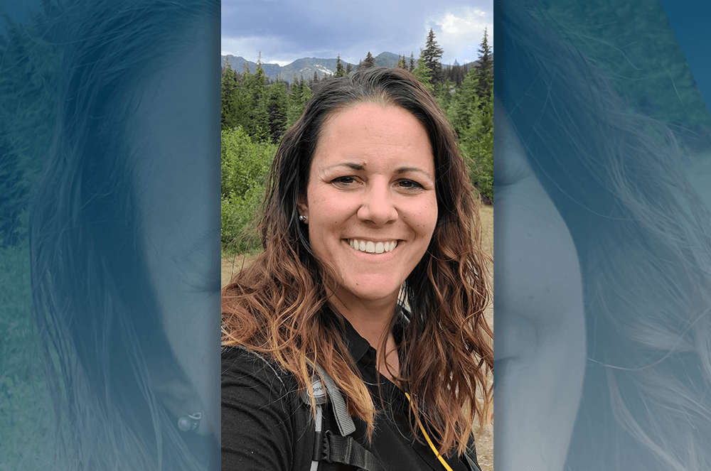 Woman smiling outdoors with mountains and trees in background