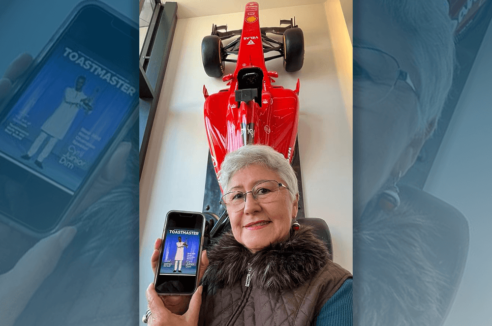Woman posing with magazine on iPhone with racecar in background