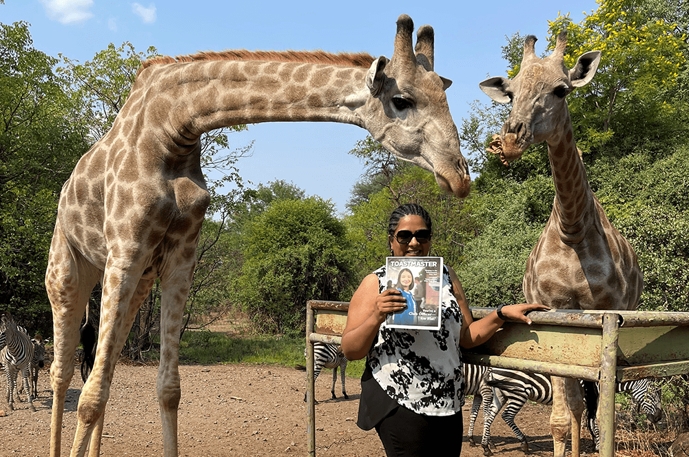 Woman holding magazine and posing with two giraffes in Zambia