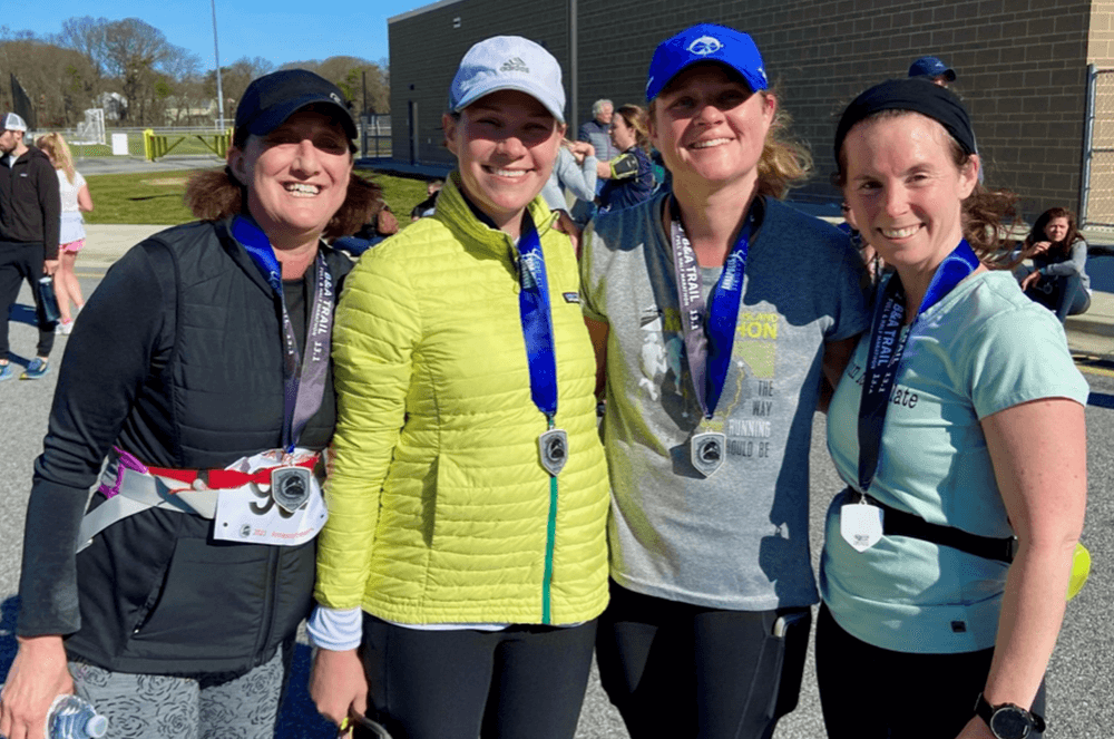 Four women wearing medals posing outside after running marathon