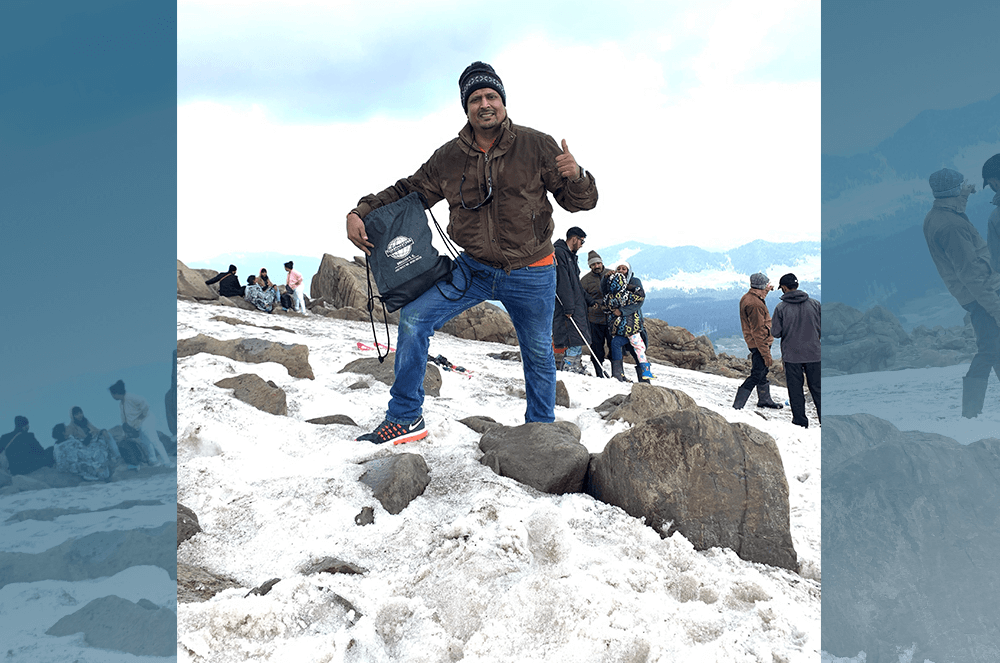 Man posing on top of mountain peak holding Toastmasters cinch
