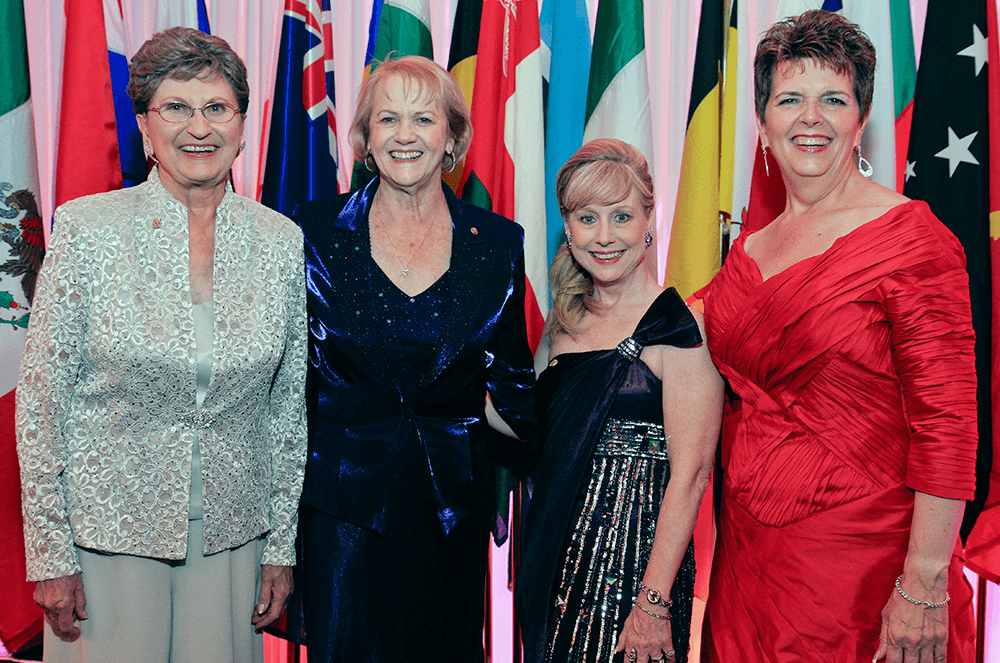Four female past international presidents of Toastmasters posing in front of flags