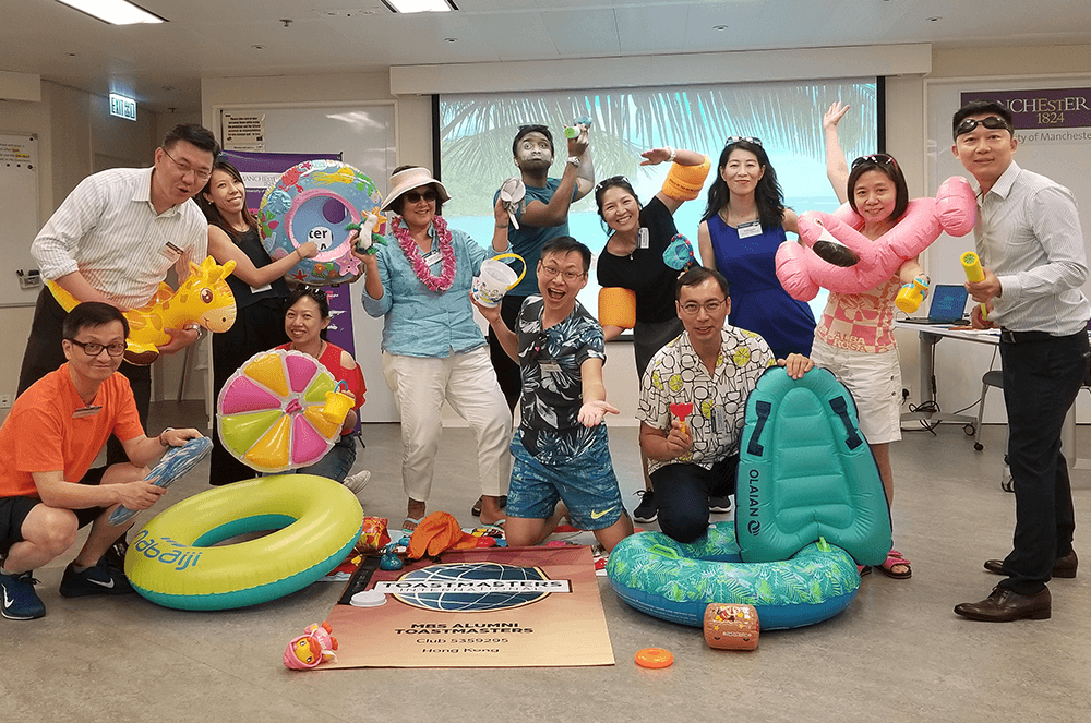 Members of the Manchester Business School Alumni Toastmasters in Hong Kong don their beach gear, including sunglasses, swim wings, and floaties, during a “beach party” themed meeting. To enhance the theme, speakers stood in front of a beach view (shown on a projector) while the sounds of ocean waves and bird calls played in the background.
