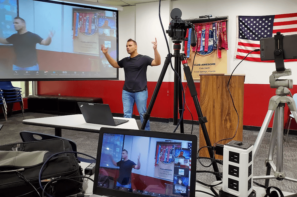 Man holding up hands while speaking to a hybrid audience