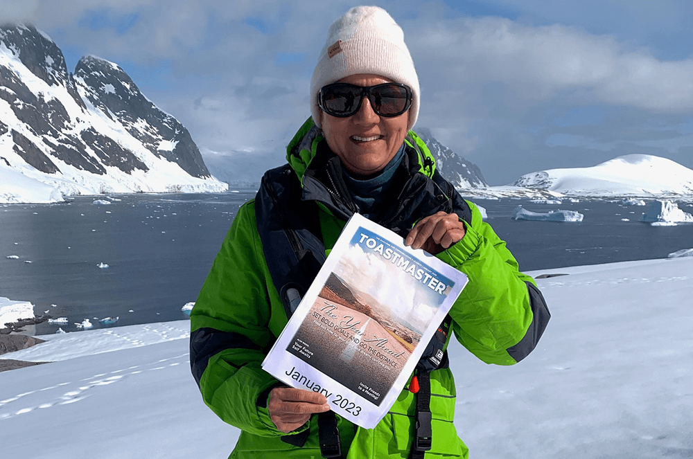 Woman in green jacket holding magazine cover while standing in snow in Antarctica