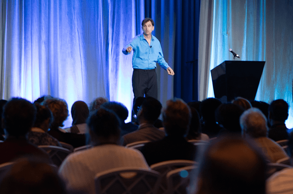 Man in blue shirt speaking to audience from stage