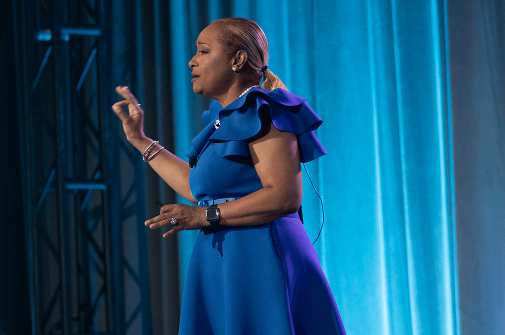 Woman in blue dress speaking onstage using hand gesture
