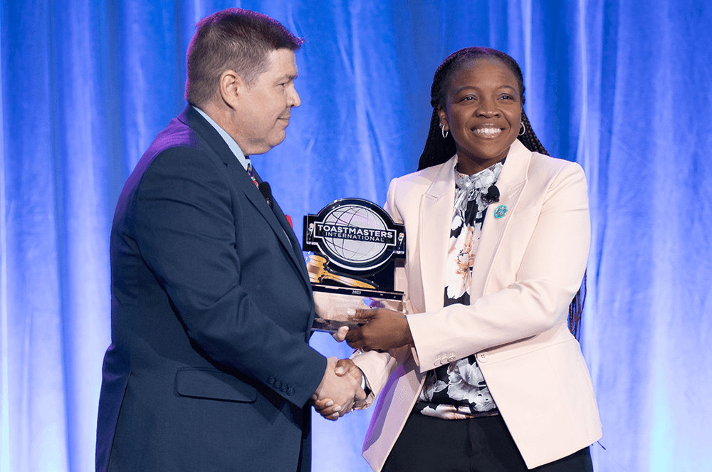 Man handing woman trophy while shaking her hand