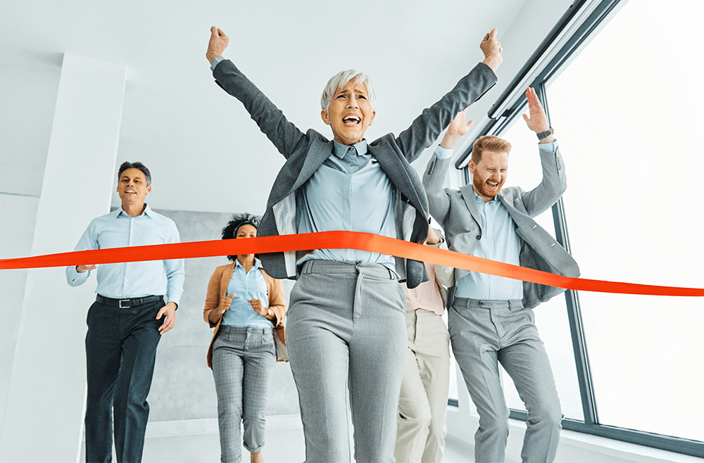 Woman in gray business suit crossing finish line through red ribbon