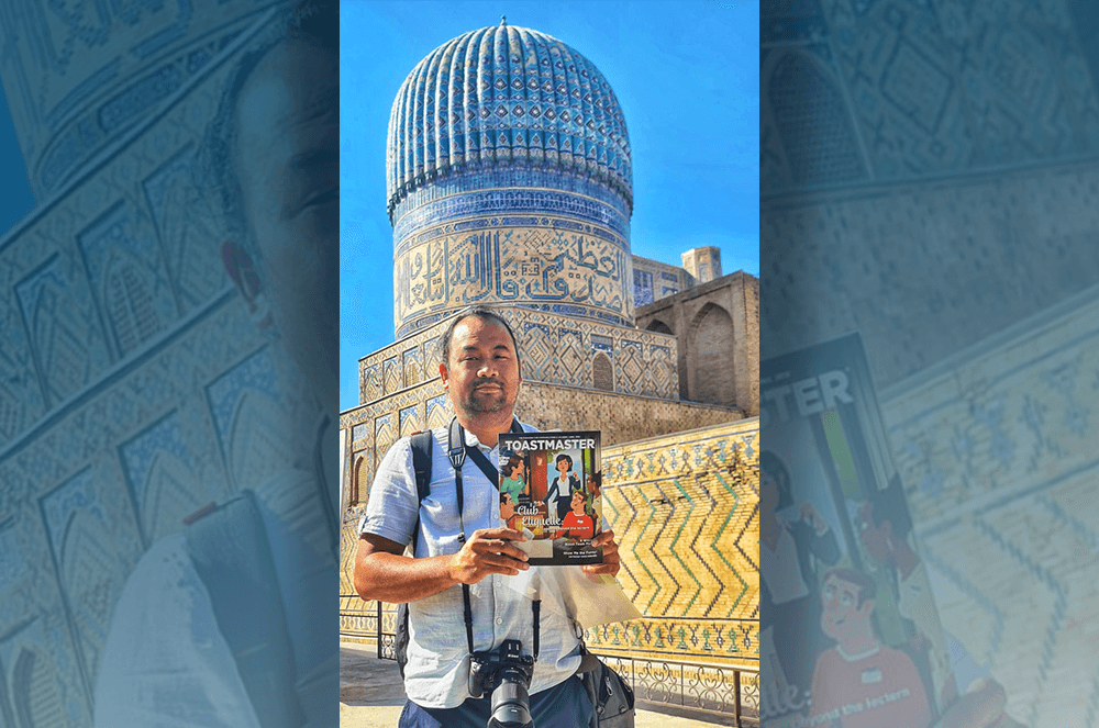 Man holding Toastmaster magazine in front of blue temple in Uzbekistan