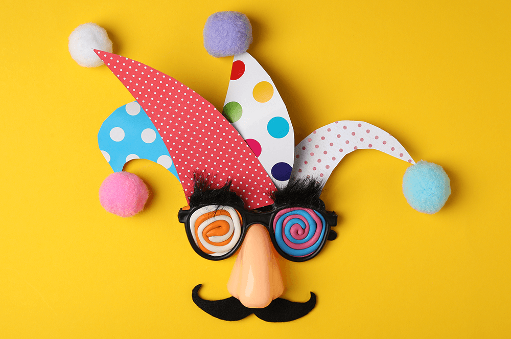 Jester hat with funny glasses, nose, and mustache on yellow background