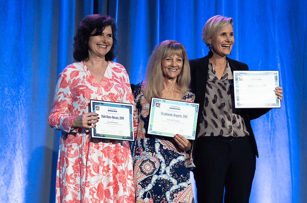 Three women holding certificates onstage at 2023 Toastmasters International Convention