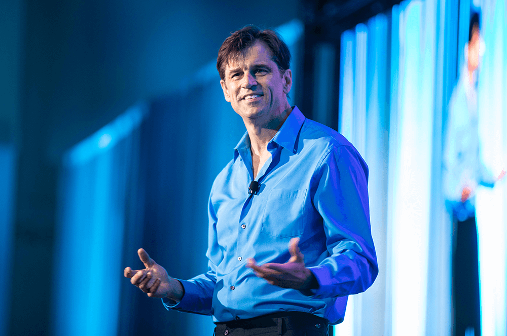 Man in blue shirt presenting onstage with blue background