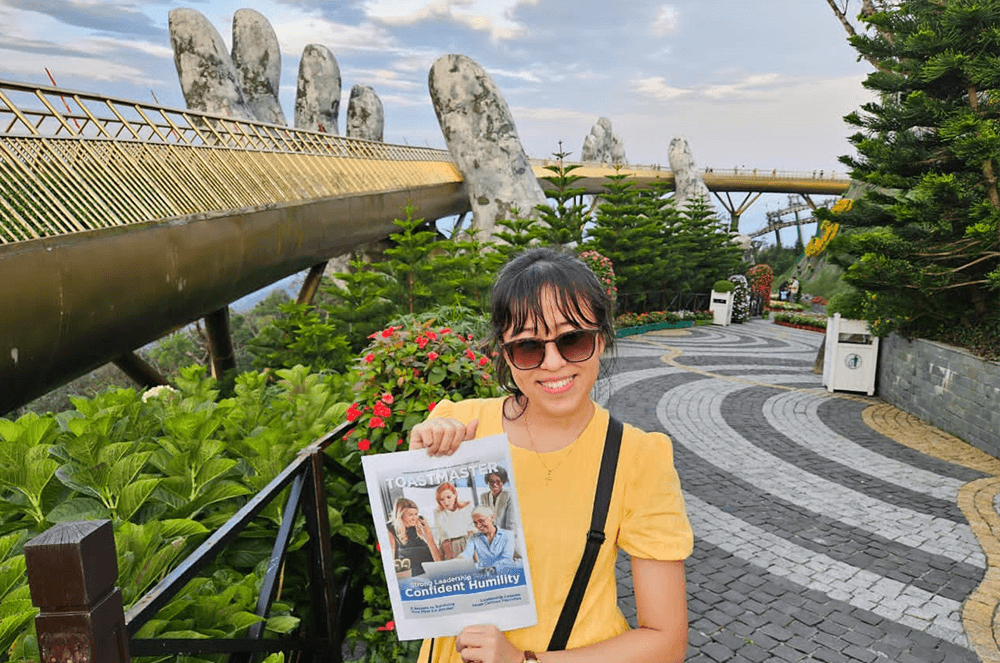 Woman in yellow shirt posing with Toastmaster magazine at Ba Na Hills