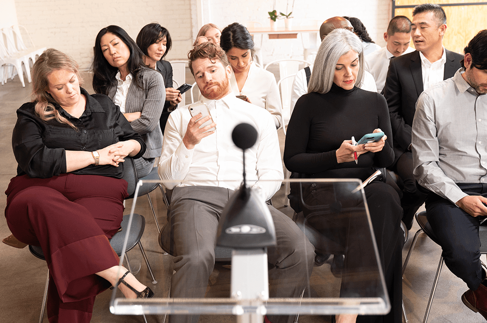 Group of men and women in audience distracted by phones