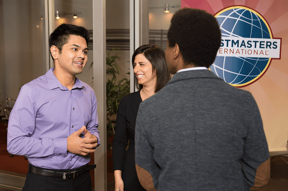 Man talking to another man and woman near Toastmasters banner