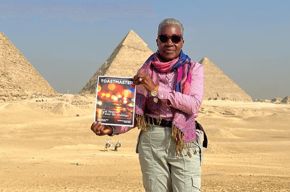 Woman in pink shirt posing with magazine cover in front of Pyramids of Giza in Egypt
