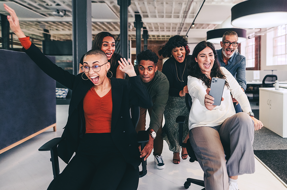 Coworkers playing in office chairs while laughing