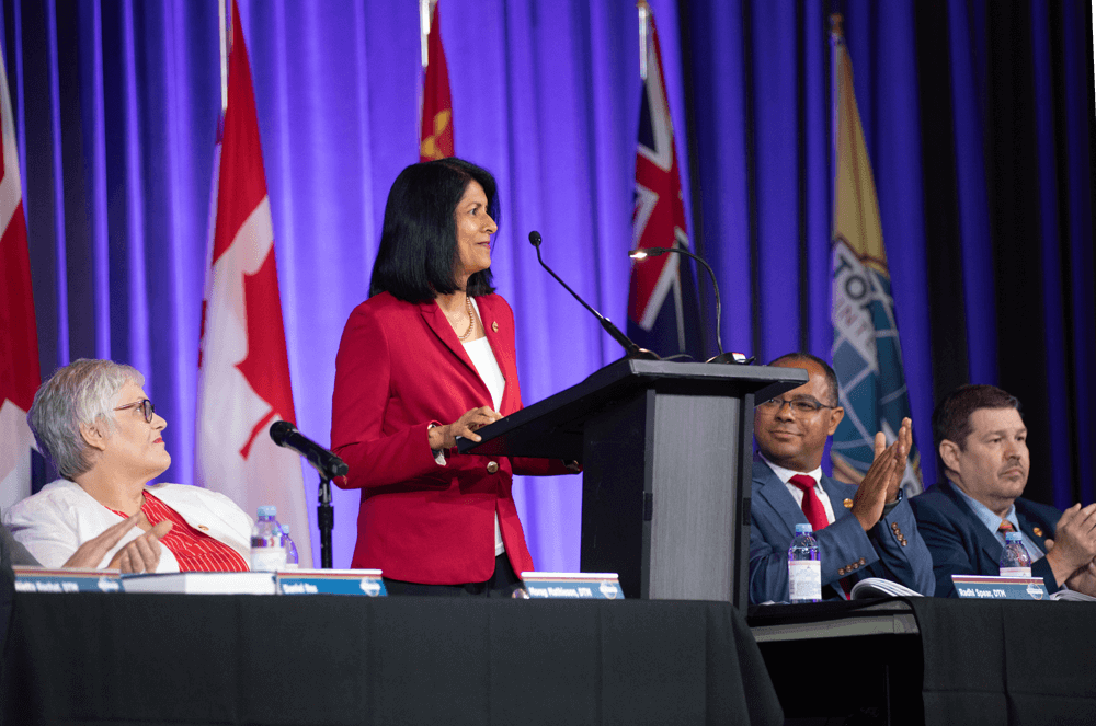 International President Radhi Spear speaking while past presidents sit at table onstage