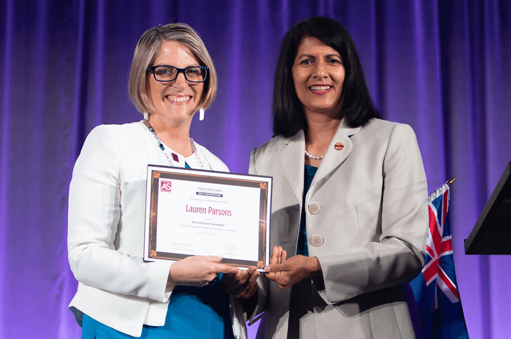 Two women posing onstage with award against purple background