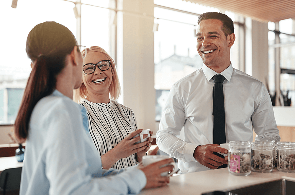 Man and two women smiling in work breakroom with coffee mugs