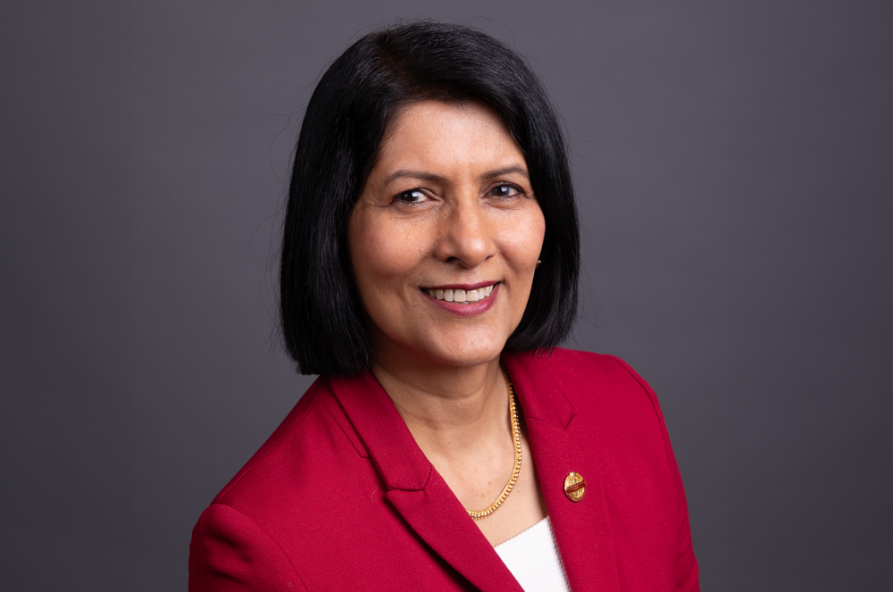 Toastmasters International President Radhi Spear in red suit jacket with Toastmasters pin