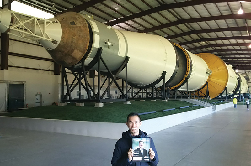 Yoshiyuki Kajikawa, ACB, ALB, from Nishinomiya-Shi Hyogo-Ken, Japan, poses near the Saturn V rocket at NASA Johnson Space Center in Houston, Texas.