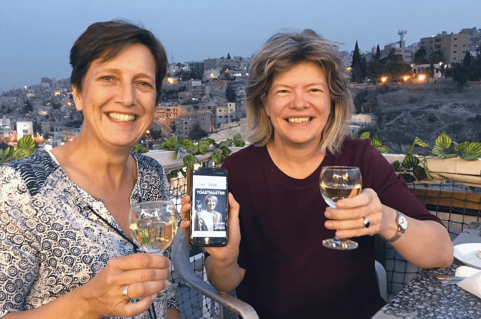 Lilian Van der Gugten, Dtm, left, and Lucy Sennef, ACS, ALB, of Apeldoorn, ­Netherlands, show the online Toastmaster ­magazine on a rooftop over­looking Amman, Jordan. 