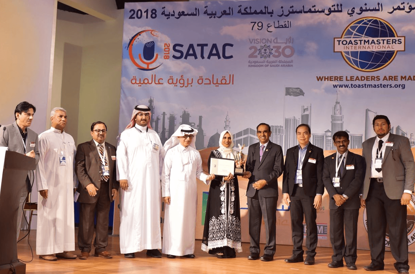 Bilquis (center) accepts a trophy and certificate from Past International President Balraj Arunasalam at District 79's 2018 conference.