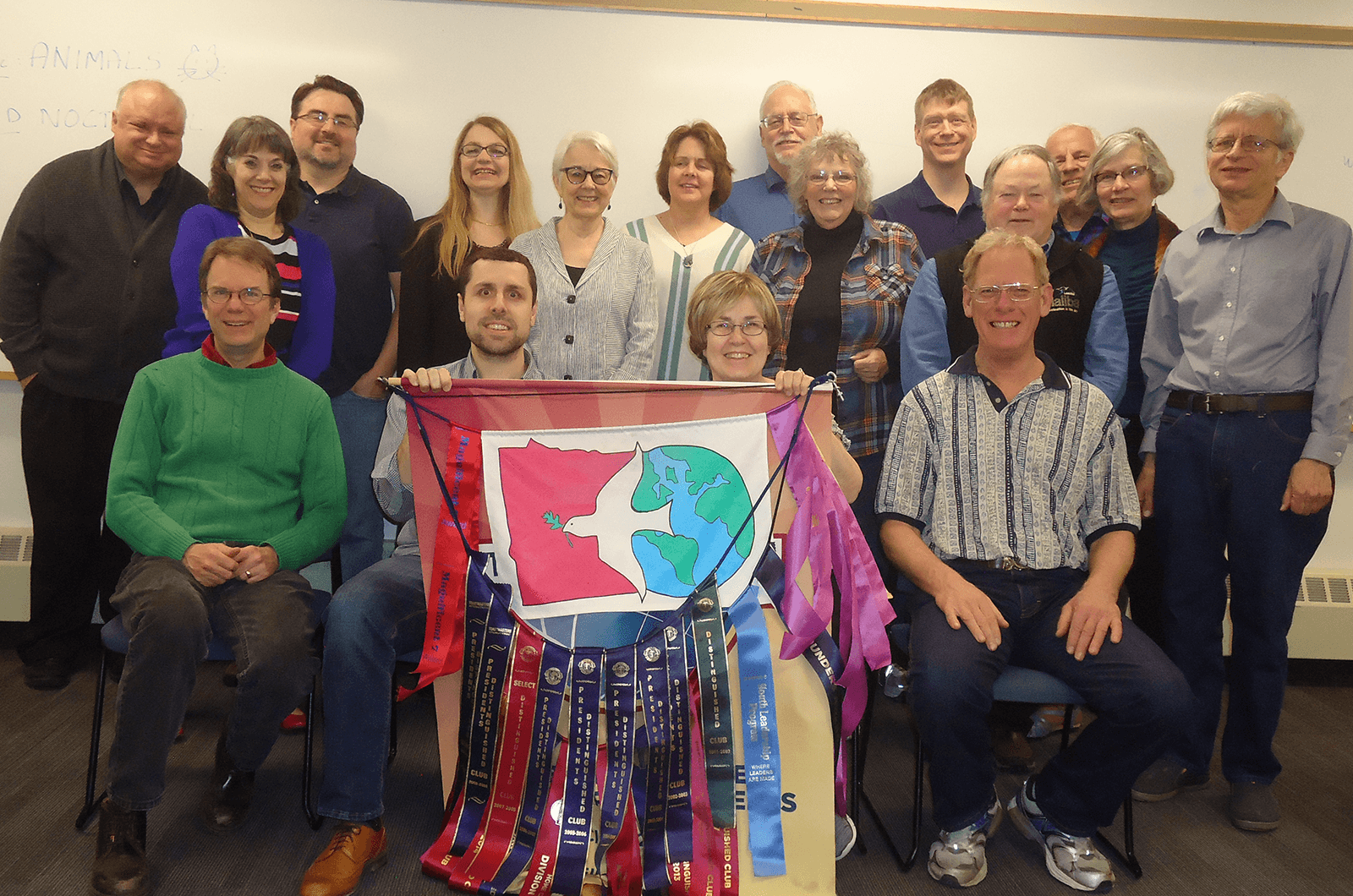 Members of the Minnesota Returned Peace Corps Volunteers Toastmasters club pose with their Toastmasters banner and Peace Corp logo.