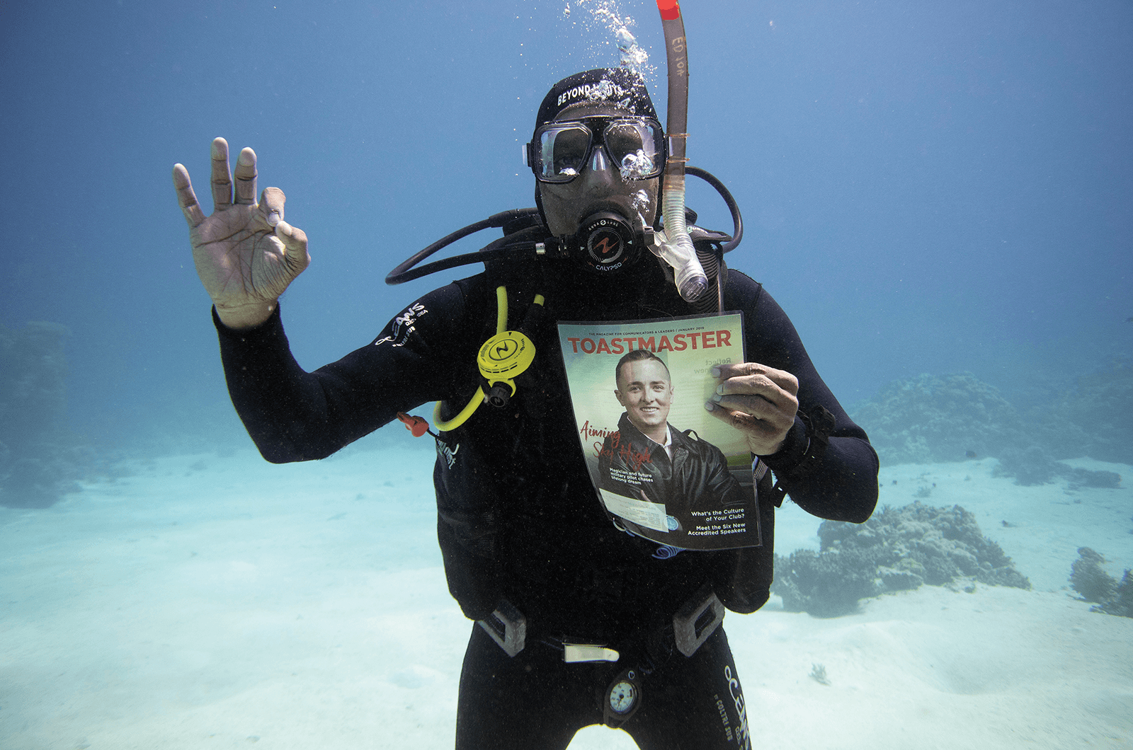 Agostinho Cajetan Barretto of Springfield Gardens, New York, takes his Toastmaster underwater while scuba diving in Sharm El Sheikh, Egypt. His hand sign is a universal scuba diving code informing those in the water that he is safe.