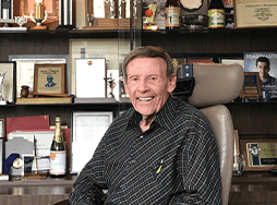 Toastmaster Burt Epstein sits in chair with awards in background