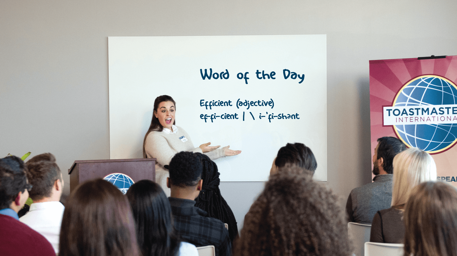 Woman stands in front of white board at Toastmasters meeting