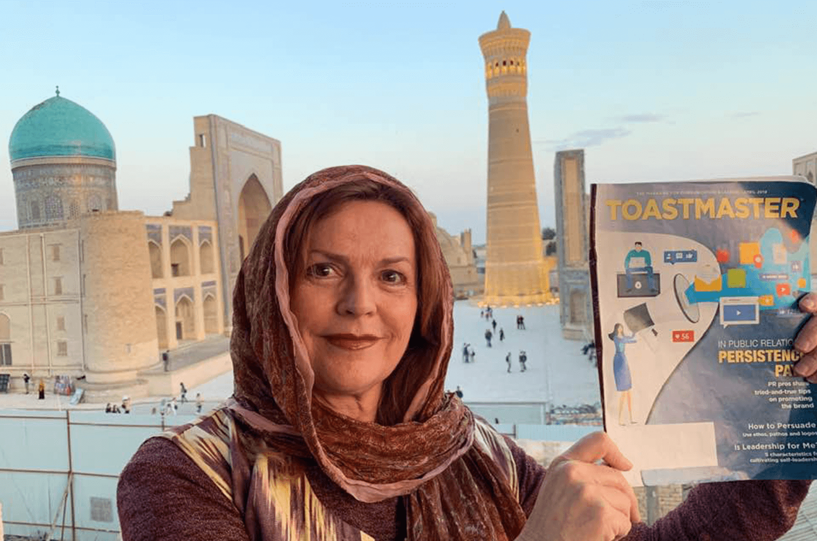 Ana González Ferrán, DTM, of Alacant, Spain, travels to Bukhara, Uzbekistan. She stands with her Toastmaster magazine in front of Poi Kalan, an Islamic religious complex. 