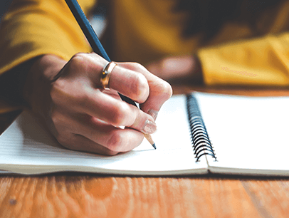 Person writing with a pencil in a notebook