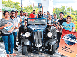 Toastmasters members holding magazine while posing next to 1927 car