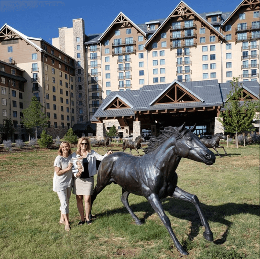 Jody Mayer of Minnetonka, Minnesota, and Michele Cooper of Hopkins, Minnesota, pose with one of the horse statues in front of the Gaylord Rockies Resort and Convention Center at the Toastmasters International Convention in Denver, Colorado.