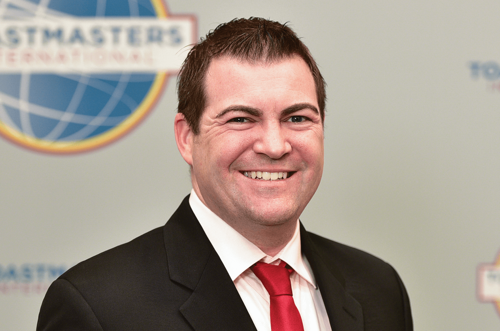Man in suit jacket and red tie smiling