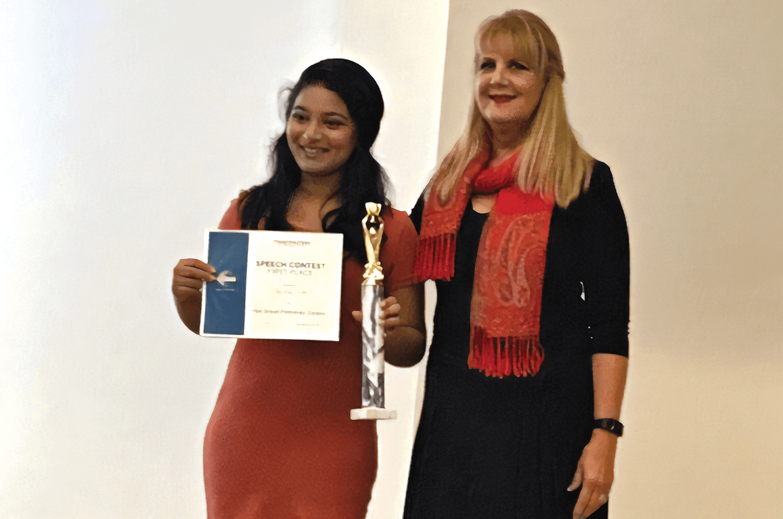Young woman holds certificate next to Toastmaster member