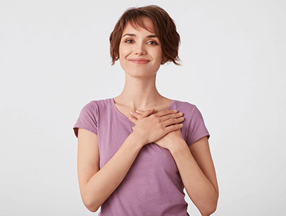 Woman in pink shirt holding hands over her heart while smiling