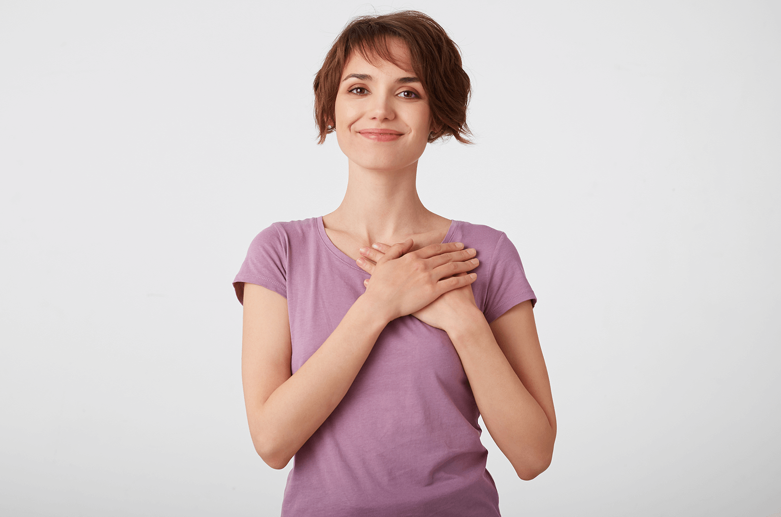 Woman in pink shirt holding hands over her heart while smiling
