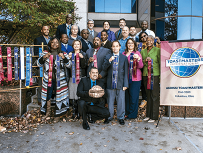 Group of Toastmasters members standing outside next to banner and ribbons