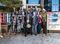 Group of Toastmasters members standing outside next to banner and ribbons