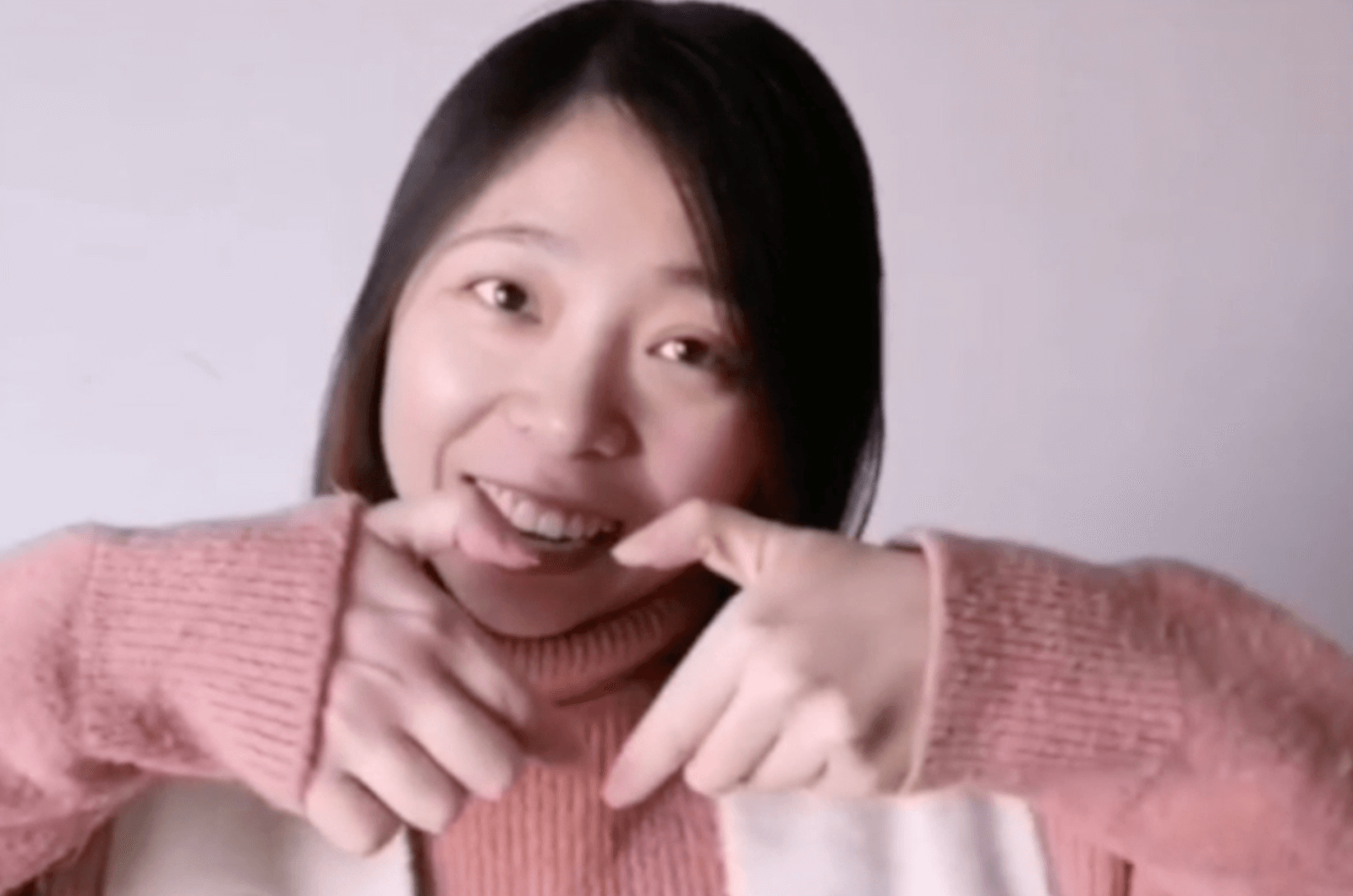 Woman in pink sweater smiling while holding up hands making a heart shape