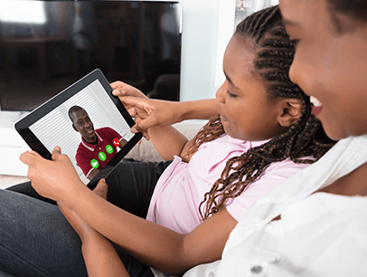 Mother and daughter sitting together and talking to male on iPad