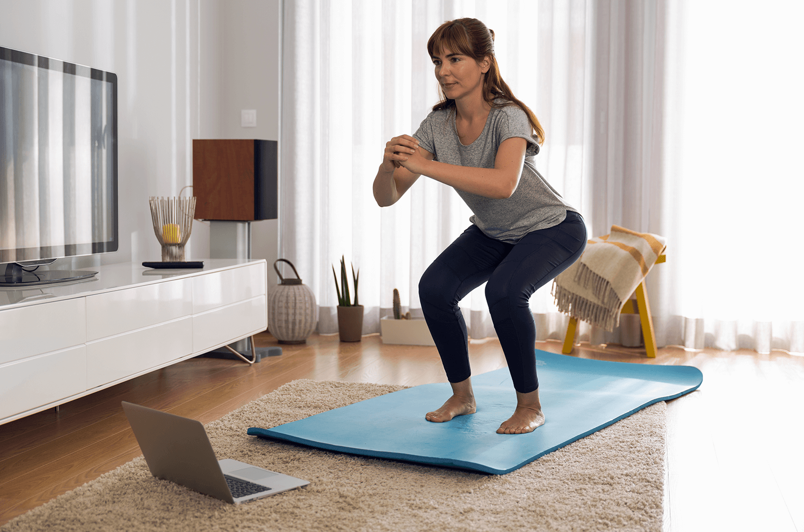 Woman watching laptop while exercising on blue mat in living room