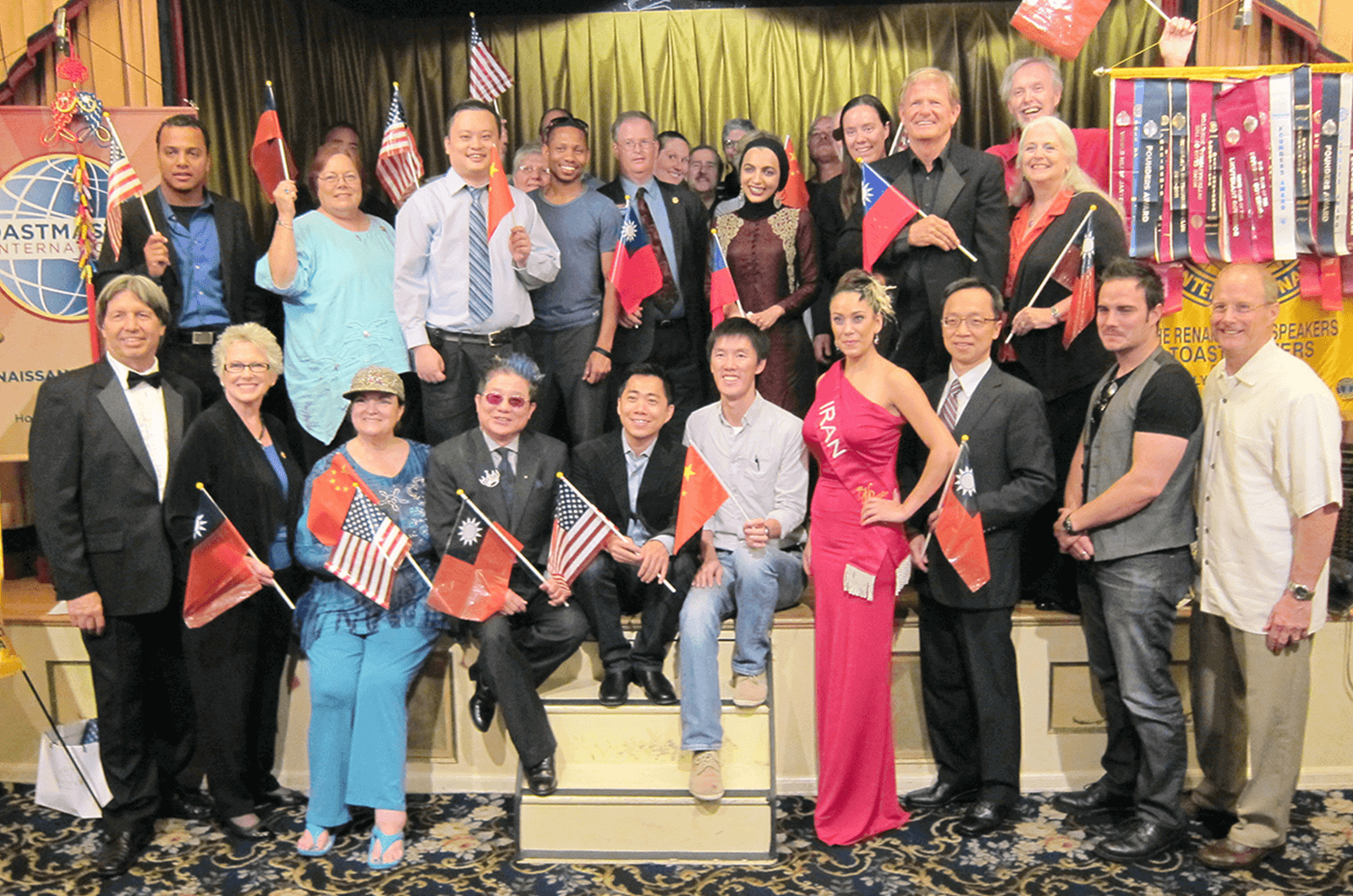 A group of members from the Renaissance Speakers Toastmasters club pose with banners and flags